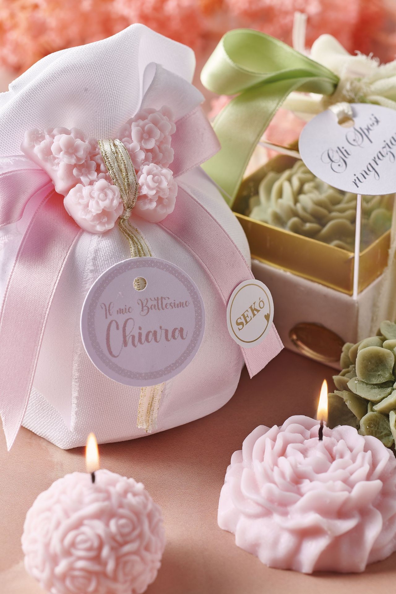 Pink and green decorative soaps with intricate floral designs and ribbon, accompanied by lit candles.